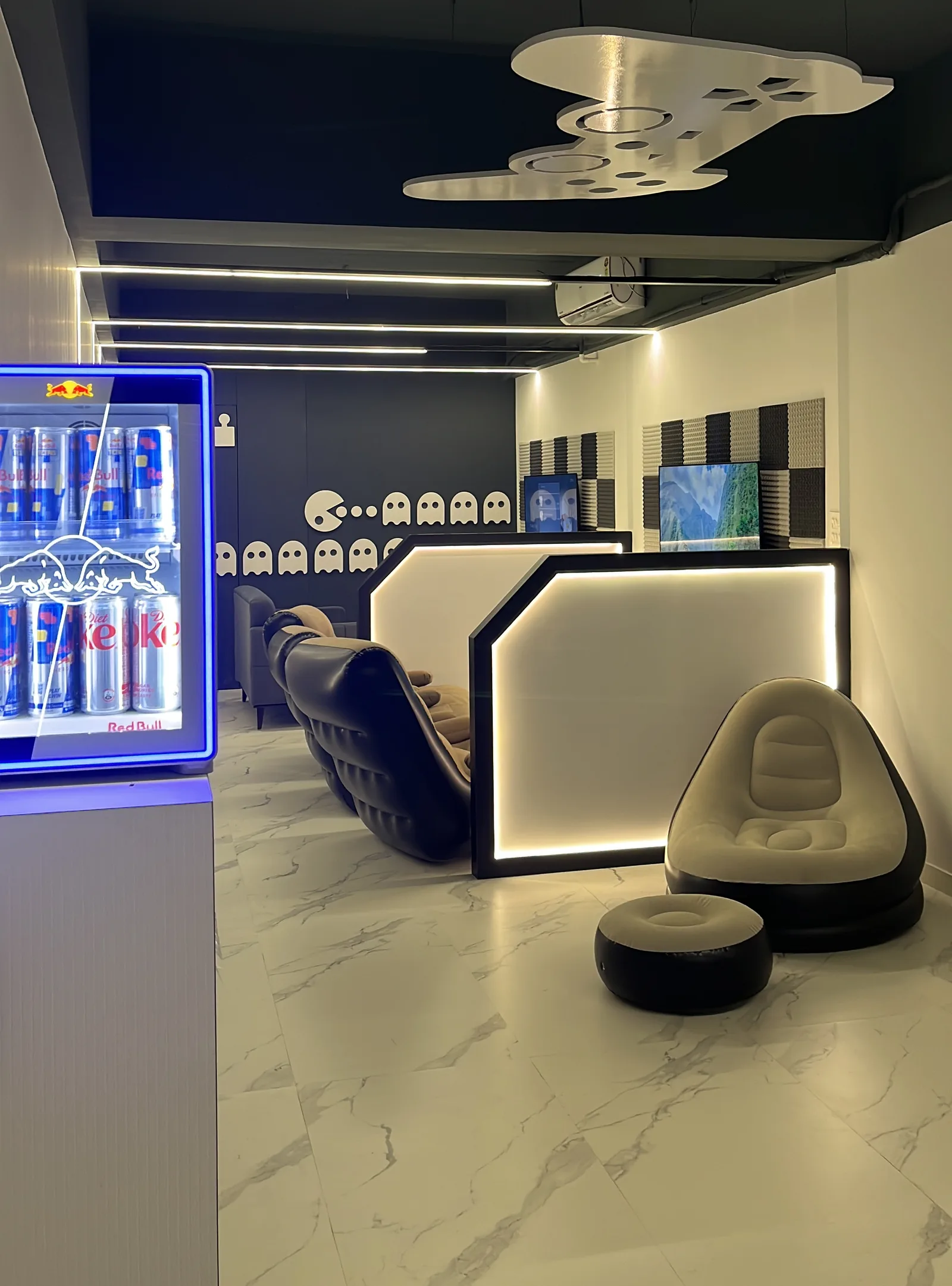 Inside Plug & Play Lounge — reception desk, Red Bull fridge and lounge seating beneath the Pac-Man wall